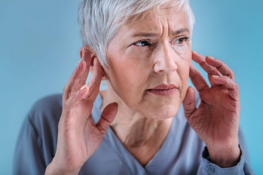 Ältere Frau hält sich mit beiden Händen an die Ohren und wirkt angespannt. Das Bild symbolisiert typische Symptome eines Hörsturzes wie plötzliches Hörvermögen-Problem, Druckgefühl im Ohr und akute Hörminderung.